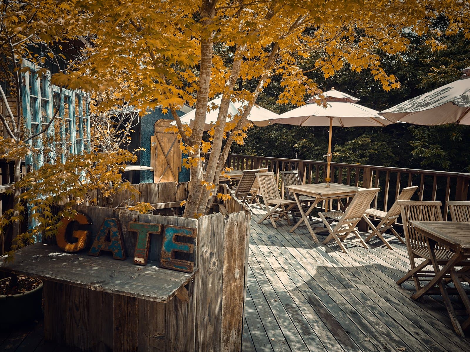 GAFLO CAFE：「GATE」の文字が置かれたウッドデッキのテラス席。パラソルの下に木のテーブルと椅子が並ぶ（2026年8月撮影）。