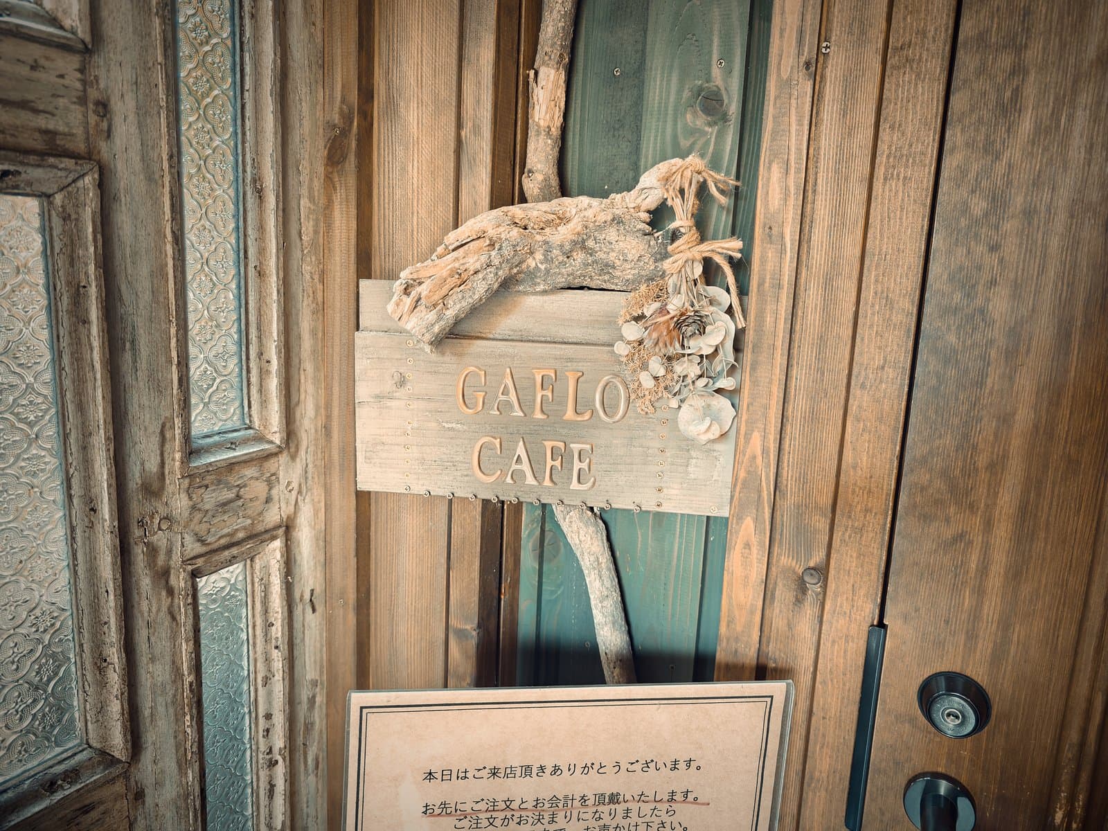 GAFLO CAFE：扉に掛かる「GAFLO CAFE」の木札。流木とドライフラワーが添えられている（2026年8月撮影）。