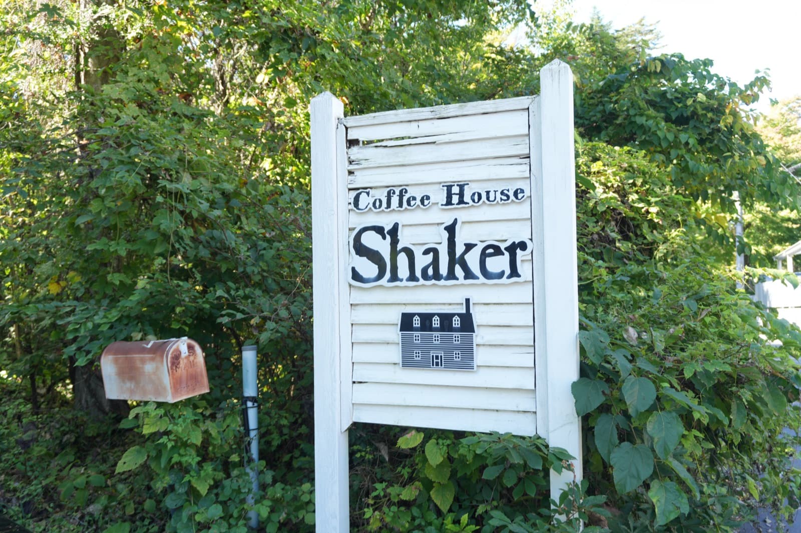 道路際に立つ「Coffee House Shaker」の看板。シェーカー様式の家の絵と古い郵便受けが目印で、これを見落とすと入口を通り過ぎる(2026年9月22日訪問)
