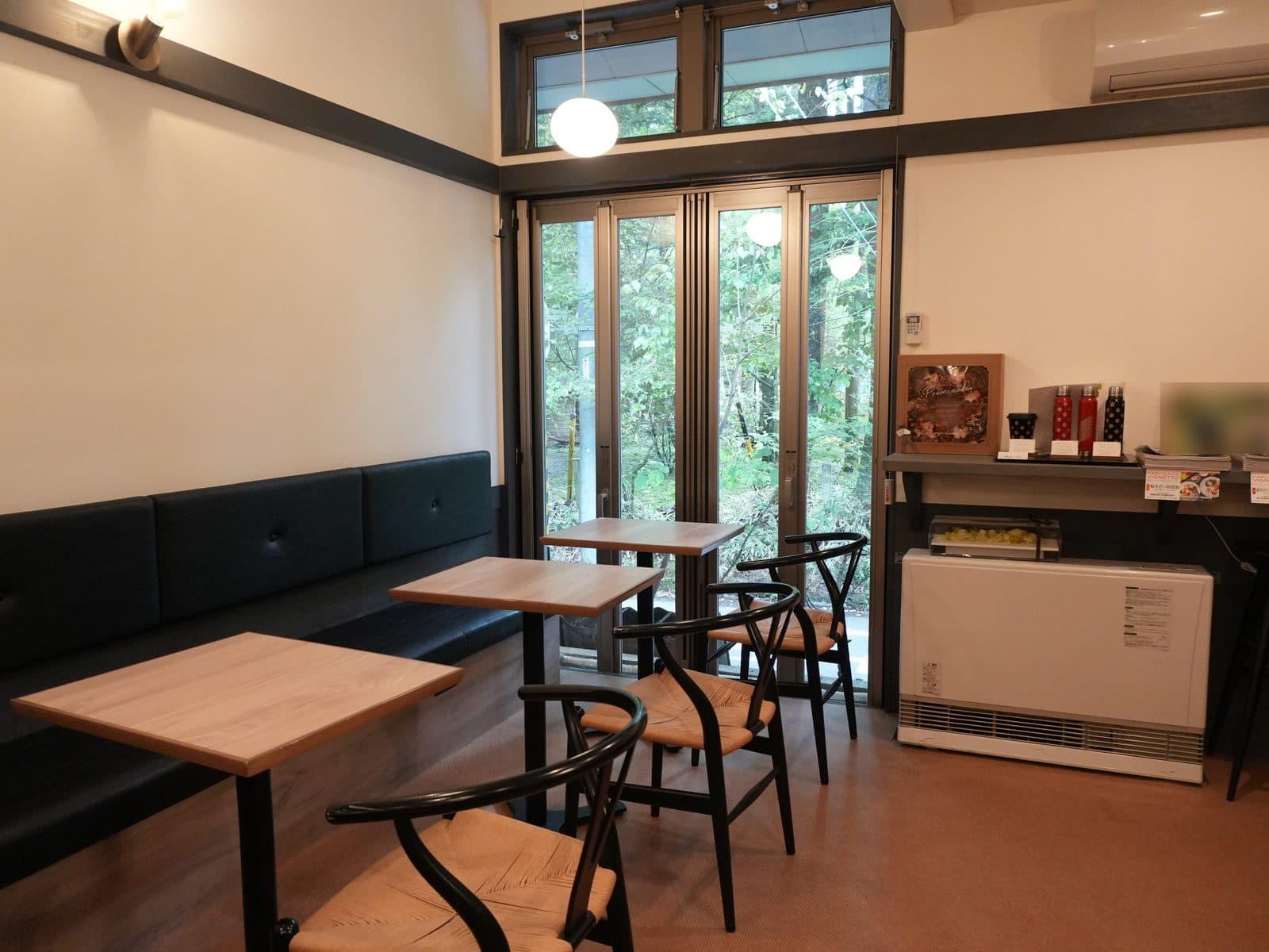 カフェ側の客席。壁沿いのソファ席と2人がけのテーブルが並び、窓の外は緑。コンセントはソファの下にあります(2026年9月19日・編集部撮影)